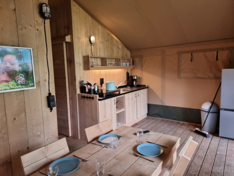 Interno di tenda safari con mobili in legno, angolo cottura e tavolo da pranzo al Camping het Horstmannsbos.