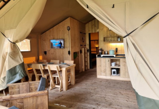 Innenaufnahme eines komfortablen Safarizelts mit Holzmöbeln und Küche bei Camping het Horstmannsbos, Niederlande.