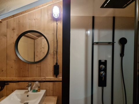 Modern safari tent bathroom at Camping het Horstmannsbos with wooden walls, sink, mirror, and shower.