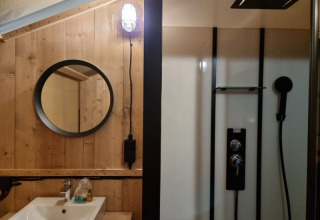 Baño moderno en una tienda safari de Camping het Horstmannsbos con pared de madera, lavabo y ducha.