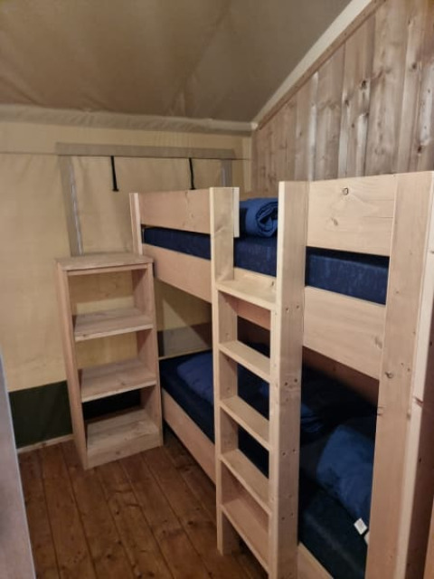 Ein Foto aus einem Safarizelt zeigt einen Raum mit Holz-Etagenbett, Regal und Holzwand.