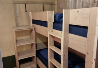 Foto uit een safaritent met een kamer voorzien van houten stapelbed, planken en houten wanden.