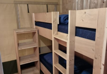 Photo from a safari tent featuring a small room with wooden bunk beds, shelves and wooden walls.