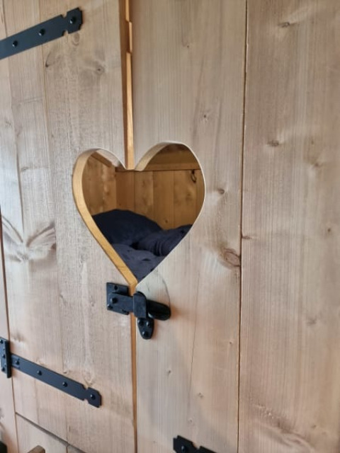 Puerta de madera con recorte en forma de corazón y herrajes negros, mostrando cama en tienda safari.