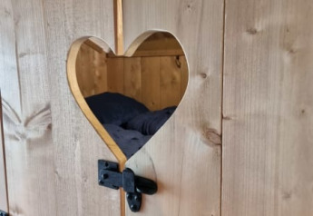 Porte en bois avec découpe en cœur et ferrures noires, vue sur un lit dans une tente safari.