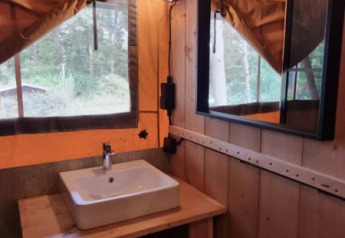 Interior de una tienda safari en Camping het Horstmannsbos, Países Bajos, con lavabo y espejo de madera.