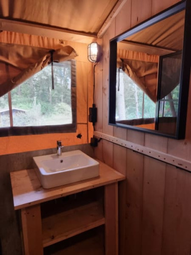Interior de una tienda safari en Camping het Horstmannsbos, Países Bajos, con lavabo y espejo de madera.
