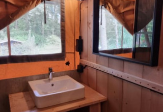 Interno di una tenda safari al Camping het Horstmannsbos, Paesi Bassi, con lavandino, specchio e arredo in legno.