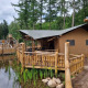 Safari-telt med sanitære faciliteter ved sø og træterrasse i frodig grøn skov, afslappende atmosfære.