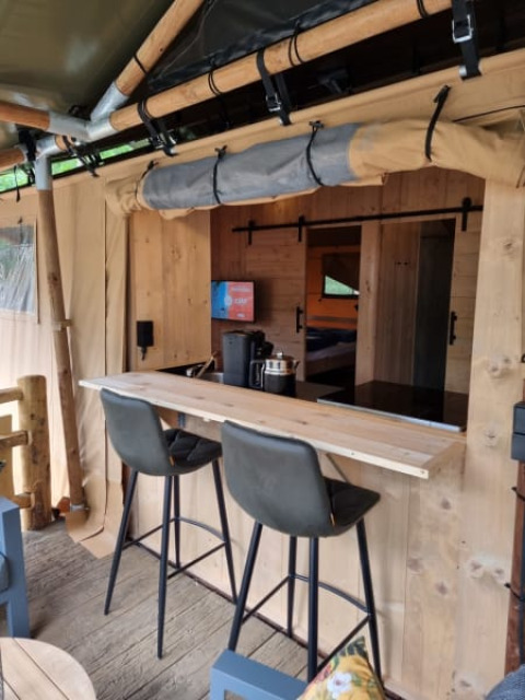 Interior view of Safari tent with private bathroom, bar area and modern chairs at Camping het Horstmannsbos, Netherlands.