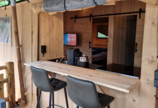 Interior view of Safari tent with private bathroom, bar area and modern chairs at Camping het Horstmannsbos, Netherlands.
