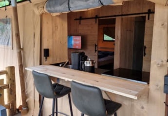 Interior view of Safari tent with private bathroom, bar area and modern chairs at Camping het Horstmannsbos, Netherlands.