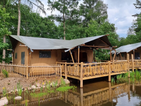 Safari tent with wooden deck over water at Camping het Horstmannsbos in the Netherlands, surrounded by trees.