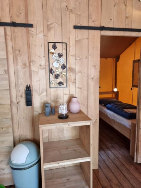 Interior view of Safari tent with wood paneled walls, shelf, and bedroom at Camping het Horstmannsbos.