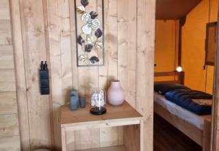 Interior view of Safari tent with wood paneled walls, shelf, and bedroom at Camping het Horstmannsbos.