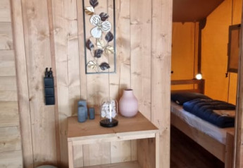 Interior view of Safari tent with wood paneled walls, shelf, and bedroom at Camping het Horstmannsbos.
