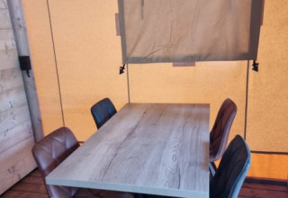 Wooden table with four chairs and a window in a canvas wall inside Safari tent + sanitary - Zeelt, Netherlands.