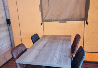 Wooden table with four chairs and a window in a canvas wall inside Safari tent + sanitary - Zeelt, Netherlands.