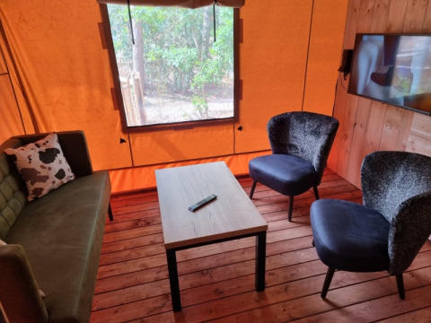 Zona de estar en tienda safari en los Países Bajos, con sillones, sofá, mesa y ventana al bosque.