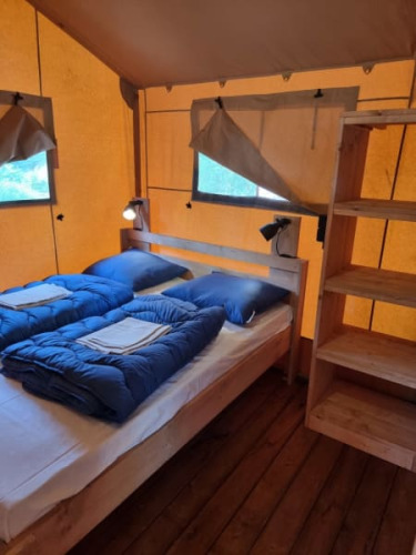 Vista interior de una tienda tipo safari con dos camas individuales, ropa de cama azul y suelo de madera en Camping het Horstmannsbos.