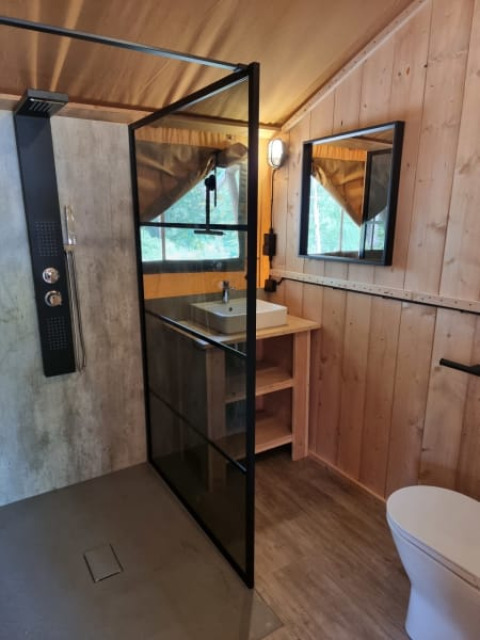 Baño moderno con mampara de vidrio, lavabo y WC dentro de una tienda safari en Camping het Horstmannsbos.