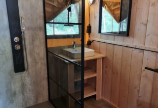 Baño moderno con mampara de vidrio, lavabo y WC dentro de una tienda safari en Camping het Horstmannsbos.