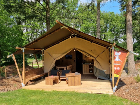 Safari-Zelt mit eigenem Bad, Holzterrasse und gemütlicher Außensitzgruppe im grünen Wald.