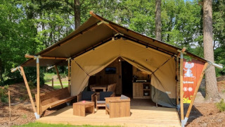 Tenda safari con servizi igienici privati, veranda in legno e zona relax all'aperto in ambiente boschivo.