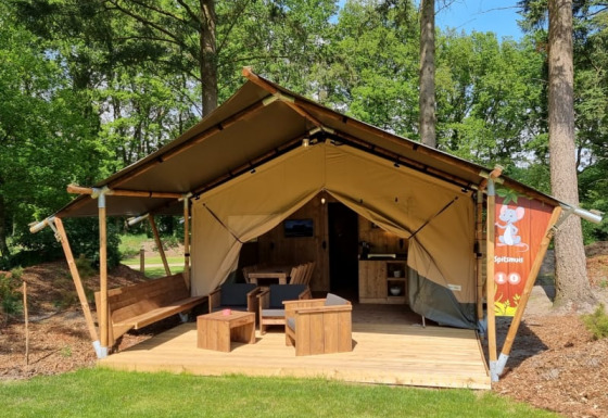 Tienda safari con baño privado, terraza de madera y zona de estar exterior en entorno boscoso verde.