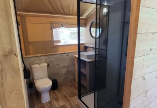 Baño en tienda safari en Camping het Horstmannsbos, Países Bajos, con ducha, inodoro y lavabo.