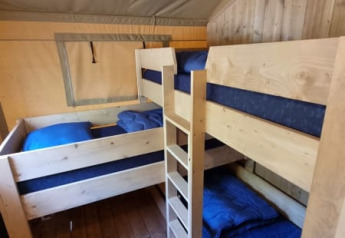 Vista interna di una tenda safari con letti a castello in legno e biancheria blu al Camping het Horstmannsbos.