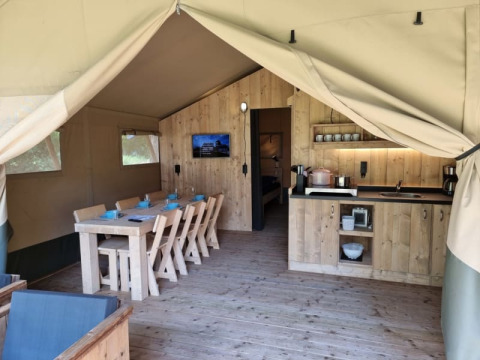 Interior de una tienda safari con comedor, cocina y muebles de madera en Camping het Horstmannsbos, Países Bajos.