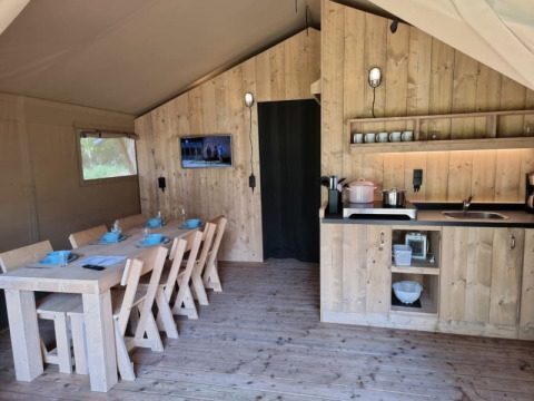 Interior de tienda safari con mesa de comedor y cocina de madera en Camping het Horstmannsbos.