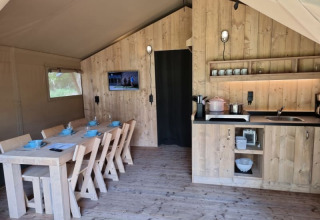 Interior of a safari tent with dining table, kitchen, and wooden decor at Camping het Horstmannsbos.