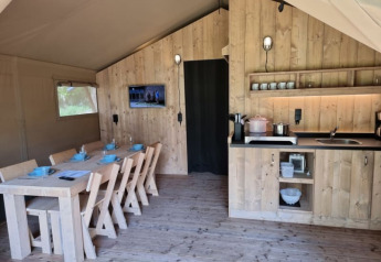Interior de tienda safari con mesa de comedor y cocina de madera en Camping het Horstmannsbos.
