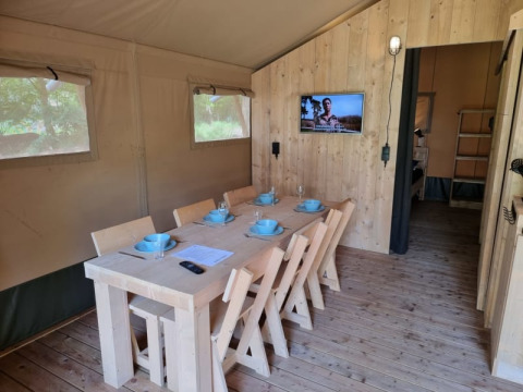 Indretning af Safari-telt med spisebord, seks stole, service og tv ved Camping het Horstmannsbos, Holland.