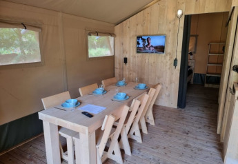 Innenraum eines Safari-Zelts mit Essbereich, TV und Holzdetails im Camping het Horstmannsbos, Niederlande.