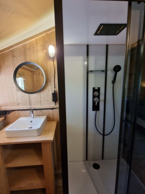 Bagno in tenda safari con doccia e lavabo al Camping het Horstmannsbos nei Paesi Bassi, legno rustico.