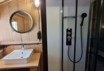 Bagno in tenda safari con doccia e lavabo al Camping het Horstmannsbos nei Paesi Bassi, legno rustico.