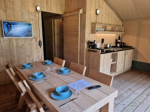 Interior of a safari tent with dining table, wooden chairs and kitchenette at Camping het Horstmannsbos.