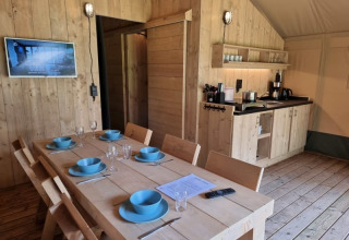 Interior of a safari tent with dining table, wooden chairs and kitchenette at Camping het Horstmannsbos.