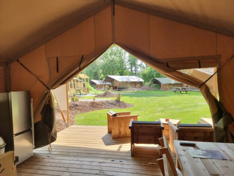 Vista desde la terraza de una tienda safari en Camping het Horstmannsbos, Países Bajos, con césped y zona de juegos.