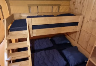 Letto a castello in legno con biancheria blu in una tenda safari al Camping het Horstmannsbos, Paesi Bassi.