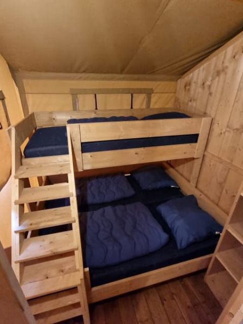Letto a castello in legno con biancheria blu in una tenda safari al Camping het Horstmannsbos, Paesi Bassi.