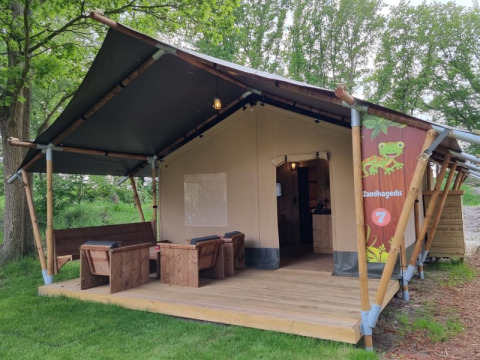 Tienda safari con terraza y muebles de madera en Camping het Horstmannsbos, Países Bajos, rodeada de naturaleza.