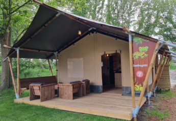 Tienda safari con terraza y muebles de madera en Camping het Horstmannsbos, Países Bajos, rodeada de naturaleza.