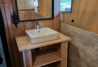 Bathroom with wooden sink stand, square basin and mirror inside a safari tent at Camping het Horstmannsbos.
