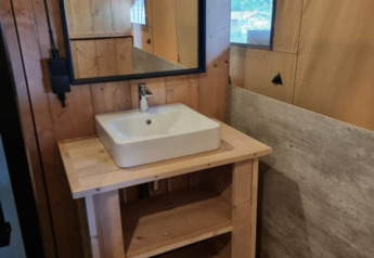 Bathroom with wooden sink stand, square basin and mirror inside a safari tent at Camping het Horstmannsbos.