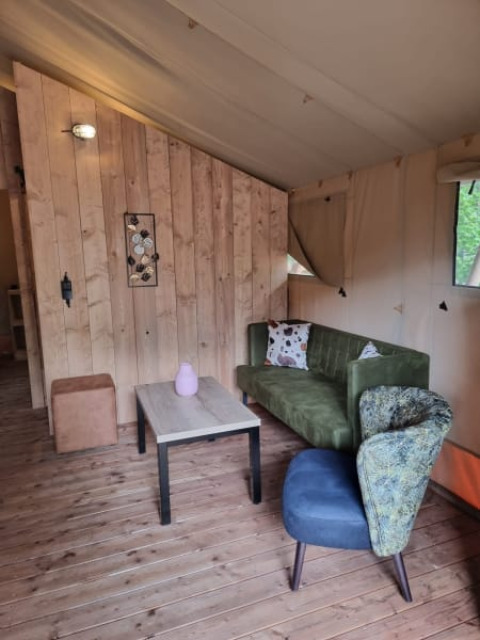 Innenraum eines Safarizelts mit grüner Couch, Tisch und Holzverkleidung in Camping het Horstmannsbos, Niederlande.