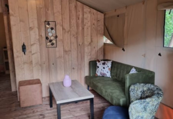 Interior of a safari tent with green sofa, colorful chair, and wooden wall at Camping het Horstmannsbos, Netherlands.